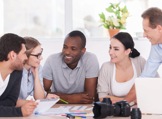 Friendly office discussion. Group of cheerful business people sitting together at the table and discussing something