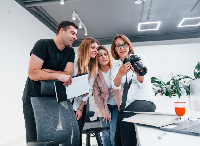 Group of business people in formal clothes indoors in the office looking at photos on the camera.